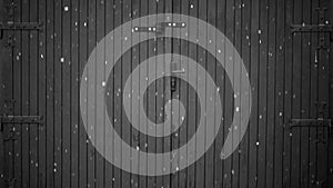 Black and white noir video of large snowflakes falling in the winter in front of an old wooden garage door with large metal hinges