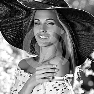 Black-white outdoor portrait of beautiful young blonde woman in black classic hat