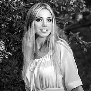 Black-white outdoor portrait of beautiful young smiling blond woman in stylish dress