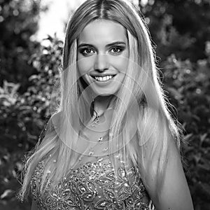 Black-white outdoor portrait of beautiful young smiling blond woman in stylish dress