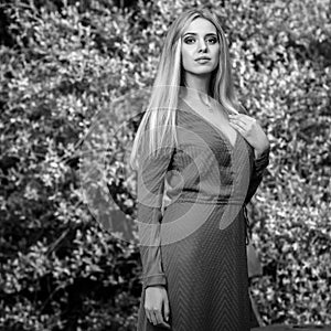 Black-white outdoor portrait of beautiful young smiling blond woman in stylish long dress