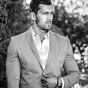 Black-white outdoor portrait of elegant handsome man in classical grey suit poses outdoor