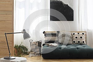 Black and white painting above scandinavian futon with pillows in trendy living room interior, real photo with mockup on the empty photo