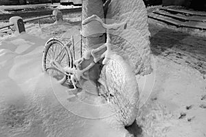 Black and white parked bike, covered with snow in the evening during a snowfall