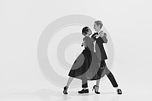 Black and white. Passion and love. Beautiful young woman and man in stylish clothes dancing on white background
