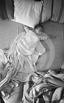 Black and white photo of baby boy sleeping on parents bed