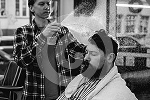 black and white photo. Barber splashes water from the spray bottle at the head hair of his client