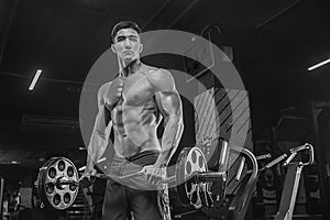 A black-and-white photo of a bodybuilder, with a modern gym, makes exercises with a barbell, with well-developed muscles, abs , b