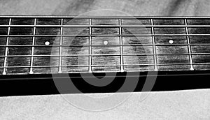 Black and white photo of a child`s acoustic guitar strings and frets on the neck of the guitar for music lessons