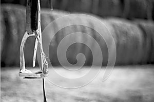 black and white photo, close up horse stirrup in the background haystacks