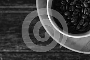 Black and white photo of coffee beans in a cup on wooden background.