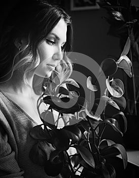 The black-white photo depicts a beautiful young woman gazing at a houseplant she has grown herself. The gardening, plant care, and