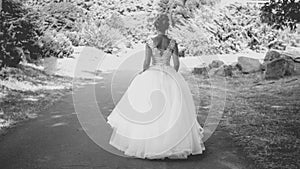 Black and white photo of elegant young bride in long dress walking at park