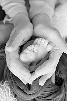 Black and white photo of the feet of a child in the arms of the mother. Macro shot. Mom and her baby. Concept of a happy family