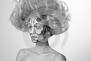 Black and white photo. Female model with colored face painted and tousled hairstyle.