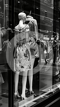 Black and white photo of glass storefronts with manikins, manikins in sold clothes