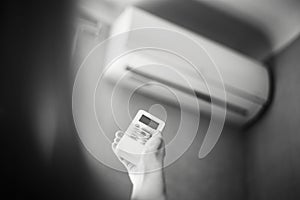 Black and white photo of hand adjusting air conditioner with remote control.