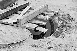 Black and white photo Hole in the ground with boards next to the hatch in the parking lot near the store.