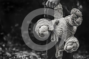 Black and white photo of Kid holding teddy waking alone in the forest, Rear view of a Boy standing alone holding his ted, Spoiled