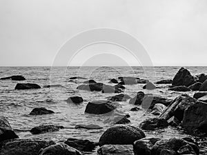 A black and white photo of large rocks rising from the sea at low tide