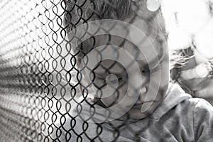 Black and white photo of a little girl with a sad look behind a metal fence, social problems, raising children in orphanages photo