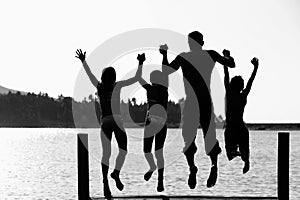 Black and white photo of man with children jumping in pier