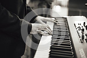 Black and white photo of man`s hand playing on electronic keyboards. Shallow depth of field. Music, entertainment