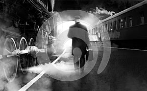 Black and white photo of man in vintage clothes walking on railway station