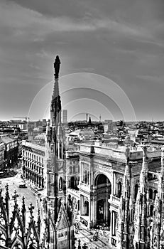 Black and white photo of marble statues of Cathedral Duomo di Milano on piazza, Milan cityscape and Galleria Vittorio Emanuele II