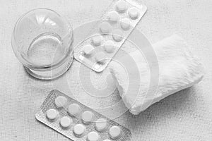 Black and white photo. Medical glass jar, gauze bandage and the currency of the tablets on a light fabric background. Retro.