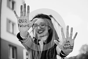 Black and white photo of modern girl with long dreadlocks and eyeglasses in nude color trench showing hands with slogan