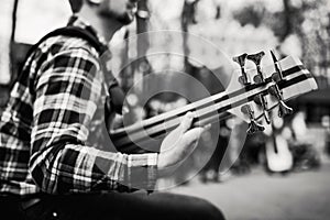 Black and white photo of musician playng on six string fretless bass guitar on the street in front of people.