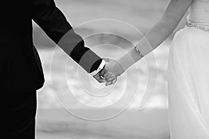 Black and white photo of a newlywed couple, groom and bride holding each others hands with rings