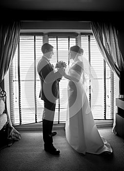 Black and white photo of newlyweds posing against window