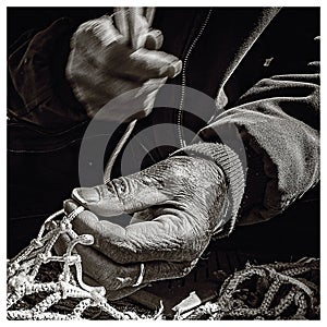 Black and white photo of an old fisherman`s hand sews a fishing net on the pier