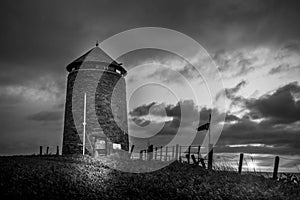 Black and white photo of an old windmill tower by the sea at night