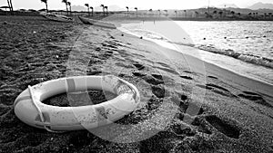 Black and white image of plastic life saving ring lying on the sea beach. Concept of safety during summer holiday