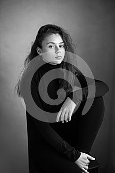 black and white photo portrait of a serious girl in black clothes in the studio.