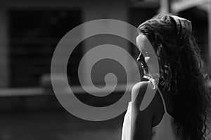 Black and white photo. Portrait of a young beautiful brunette girl with long curly hair in the street near a summer terrace cafe