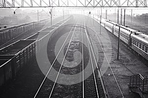 Black and white photo of railway tracks in fog with passenger and freight trains.