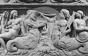 Black and white photo of sculptures carved on an ancient wall showing naked women and male sirens in the sea