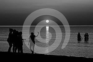 Black and white photo of silhouettes of teenagers playing in the sea during sunset