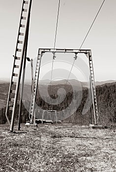 Black and white photo of a ski lift in the mountains and a background of spruce forest