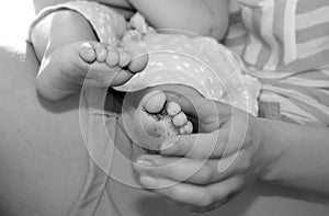 Black-and-white photo of small baby feet in mother`s palms