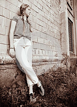 A black-and-white photo of a teenage girl with two pigtails in a checked blouse standing against the brick wall