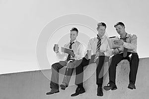 Black and white photo of thoughtful businessmen sitting while using digita tablet in office rooftop