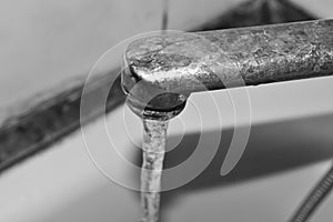 Black and white photo. Water runs from the rusty tap. Old faucet in the bathroom. The texture of the water.