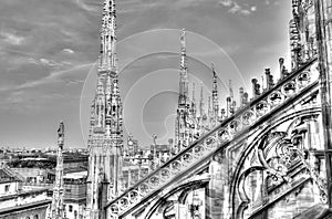 Black and white photo of the white marble statues, spires and stone sculptures on the roof of famous Cathedral Duomo