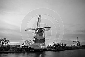 Black-white photo of windmills and water canal on sunset in Kinderdijk, Holland