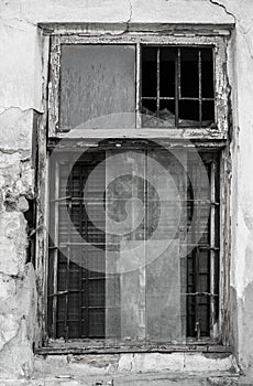 Black and white photo of an window frame with partially broken windows and metal bars inside the old dilapidated wall